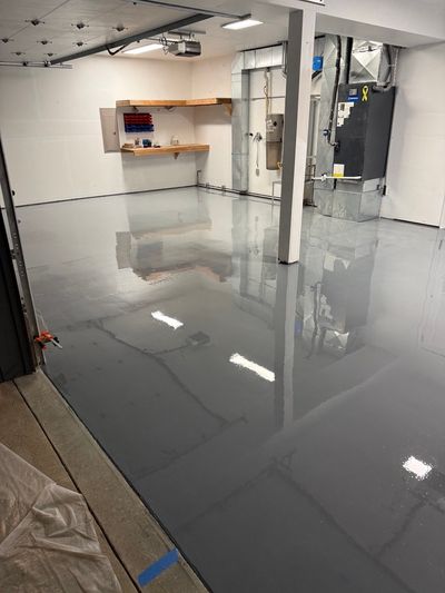 Wet gray base coat freshly rolled across the same garage floor, reflecting the ceiling lights