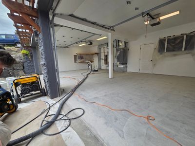 Garage slab ground back to bare concrete, with a grinder and dust extraction hose running out to the driveway